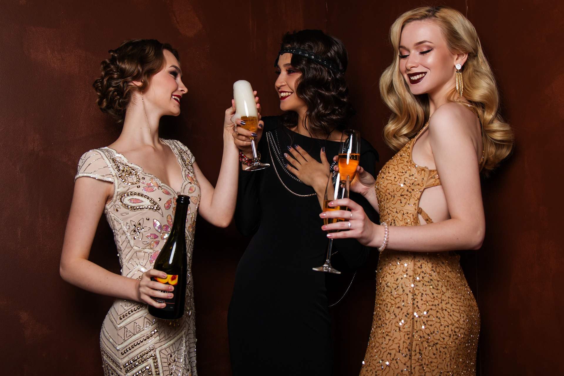 Drei Damen im Abendkleid stoßen mit Getränken an.
